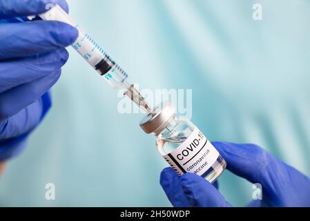 Il medico le mani nei guanti di sicurezza preparazione della siringa per l'iniezione del vaccino del coronavirus Foto Stock