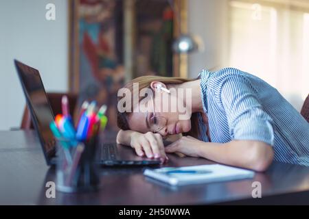 Giovane donna d'affari caucasica stanca che dorme sulla scrivania in ufficio a casa Foto Stock