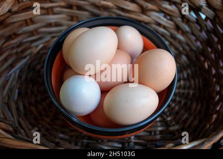 Uova crude in una piccola ciotola in un cestino più grande, appena raccolte e pronte per essere consumate, ingrediente alimentare altamente nutriente con usi diversi Foto Stock