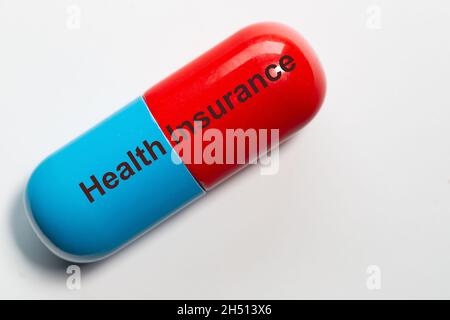 Una pillola in blu e rosso come una foto smbol ha le parole assicurazione sanitaria su di esso. La pillola è isolata su sfondo bianco. Foto Stock