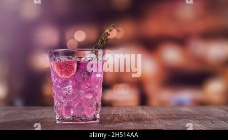 Cocktail di fichi rosa in autunno o in inverno in calice martini su un bancone bar. Cocktail di fico con timo e cubetti di ghiaccio. Messa a fuoco selettiva Foto Stock