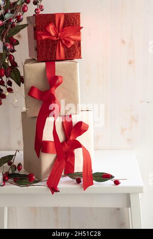 Tre regali di Natale accatastati in una torre su sfondo bianco con un bordo di bacche rosse e luci di natale con spazio copia Foto Stock