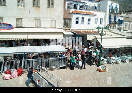 Isola di Hydra - Grecia - Maggio 21 2018 : fronte porto occupato con passeggeri in fila per salire a bordo del traghetto locale tipico porto greco scena in una giornata estiva LAN Foto Stock