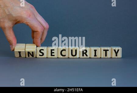 Simbolo di sicurezza o insicurezza. L'uomo d'affari trasforma i cubi di legno, cambia le parole insicurezza in sicurezza. Bellissimo sfondo grigio. Business, sicurezza o. Foto Stock