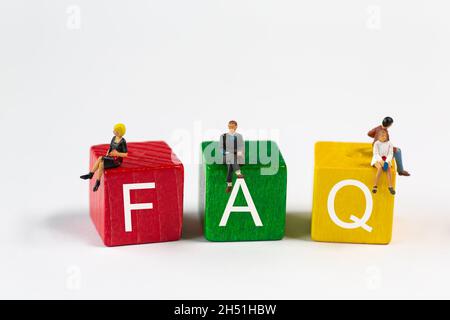 FAQ - l'abbreviazione di Frequently Asked Questions (Domande frequenti) è in caratteri bianchi su blocchi da costruzione rossi, verdi e gialli. Piccole figure di plastica si siedono sui blocchi Foto Stock