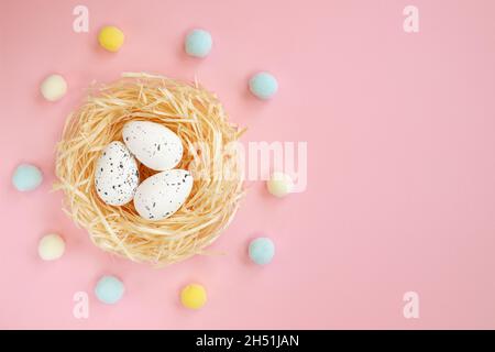 primo piano di uova di pasqua in nido d'uccello su sfondo rosa con spazio vuoto per il testo, vista dall'alto, concetto di pasqua Foto Stock