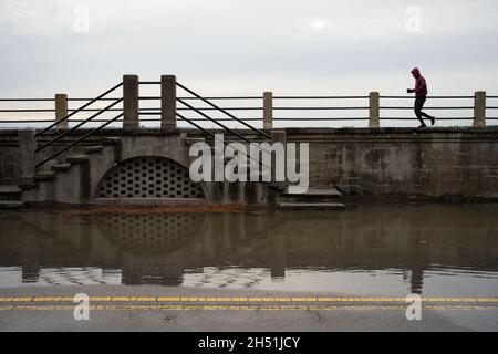 Charleston, Stati Uniti. 05 novembre 2021. Un pareggiatore corre lungo la batteria adiacente ad una parte inondata East Bay Street. Alcune parti del centro di Charleston hanno subito un secondo giorno di alluvione. La combinazione di un sistema di tempesta offshore e di una marea re insolitamente alta ha portato a diverse chiusure stradali in tutta la regione. La città sta soppesando i costi di realizzazione di un nuovo muro marino per combattere il crescente problema delle inondazioni. (Foto di Kit MacAvoy/SOPA Images/Sipa USA) Credit: Sipa USA/Alamy Live News Foto Stock