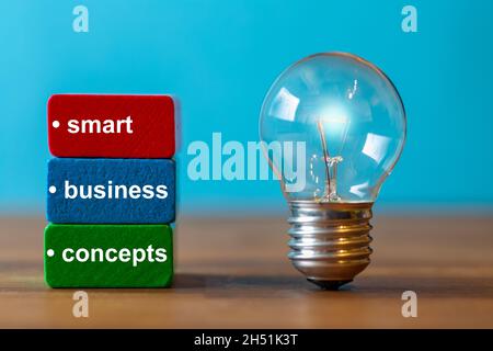 smart, business, conzepts, si trova su blocchi colorati accanto a una lampadina vintage su un piatto di legno scuro con uno sfondo blu Foto Stock