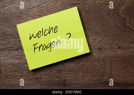 La domanda in tedesco: Quali domande? È possibile trovare su un adesivo di nota giallo autoadesivo diagonalmente su un tavolo di legno scuro con mano stilizzata Foto Stock