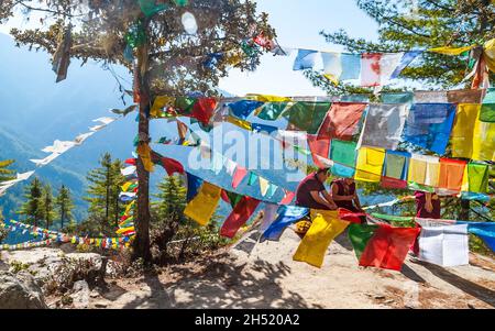 Paro, Bhutan - Febbraio 2016: Monaco buddista in abiti rossi tradizionali e preghiera multicolore bandiere buddiste tibetane Lung Ta in Himalaya sulla strada per Foto Stock