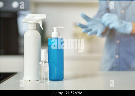 Bottiglie igienizzanti per pulire le superfici della cucina. Donna che indossa guanti protettivi mentre si prepara per la pulizia dello sfondo. Antisettico Foto Stock