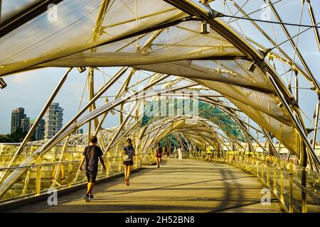 Tour turistico o locale a piedi attraverso il ponte Helix a Marina Bay durante il tramonto. Foto Stock