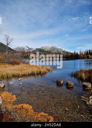 Vista autunnale del lago Strbske Pleso con acque cristalline, pali di legno e vette degli alti Tatra in Slovacchia. Foto Stock