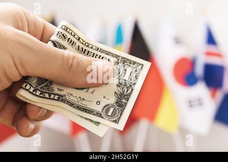Un dollaro in mano sullo sfondo delle bandiere di diversi paesi, il concetto di valuta di riserva mondiale Foto Stock