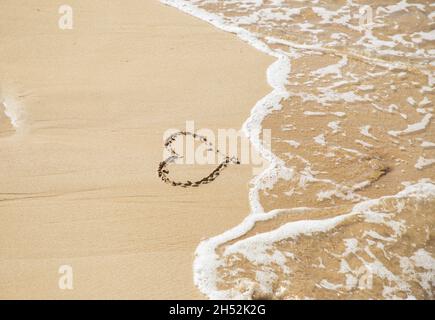 simbolo del cuore disegnato sulla sabbia sulla costa del mare. Onda in arrivo. Ciao estate. Vacanza, riposo, amore. San Valentino Foto Stock