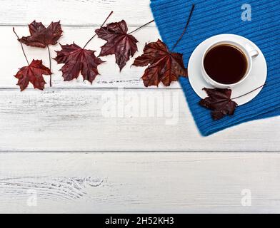 Tazza di caffè e sciarpa su sfondo di legno. Foglie cadute di acero rosso. Foto Stock