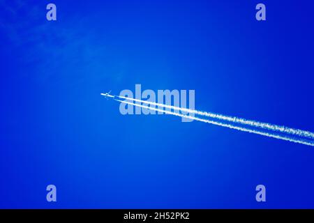 Un aereo passeggeri vola contro un cielo blu. Traccia bianca dalle turbine del velivolo. Sfondo. Foto Stock