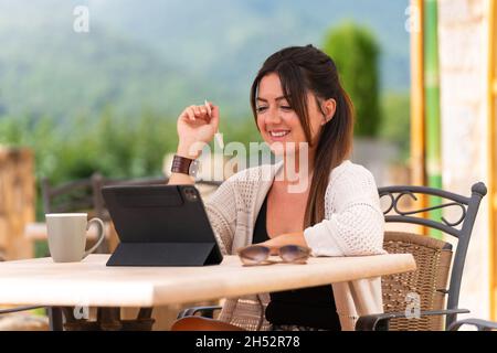 Donna seduta su una terrazza scrivendo su un tablet con penna digitale Foto Stock