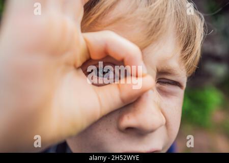 Primo piano di vista del ragazzo bianco carino che gioca all'aperto nel prato estivo, Kid che fa binoculare o eyeglasses gesto usando le sue dita Foto Stock