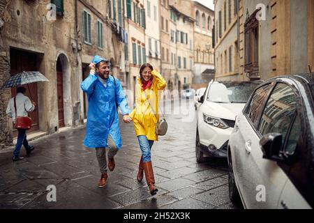 Una giovane coppia di impermeabili tiene le mani e cammina per la città in un'atmosfera tranquilla durante una pioggia. Passeggiata, pioggia, città, rapporto Foto Stock