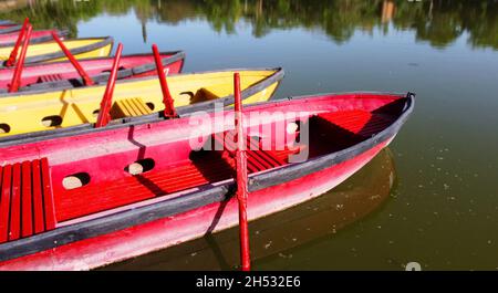 Barche a remi d'epoca rosse e gialle su acqua verde di riserva che riflettono gli alberi di un parco Foto Stock