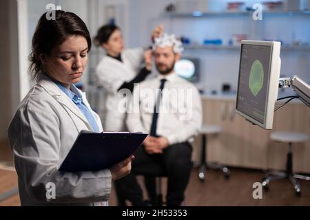 Neurologo medico donna regolazione eeg cuffia monitoraggio dell'attività cerebrale del paziente durante l'esperimento medico in laboratorio moderno. Ingegnere scienziato che analizza il sistema nervoso Foto Stock