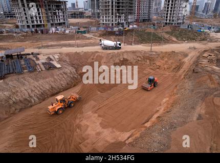 Compattatore per terreno il terreno livellante per la costruzione della fondazione. Il rullo vibra comprime il terreno per la fondazione della cassaforma. Pala caricatrice gommata su terreno Foto Stock