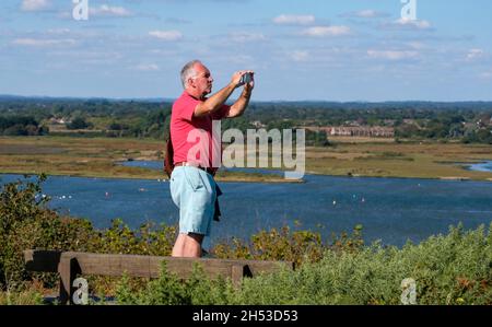 Uomo in piedi scattando una foto di una vista da Hengistbury Head in una giornata di sole nel Dorset Foto Stock