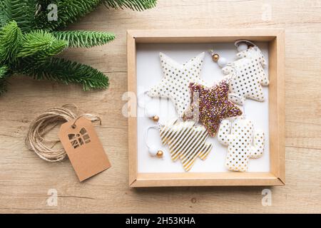 Confezione regalo con giocattoli di Natale in tessuto, rotolo di carta kraft, ramo di abete su sfondo di legno. Concetto di imballaggio ecologico, senza sprechi. Confezione regalo Foto Stock