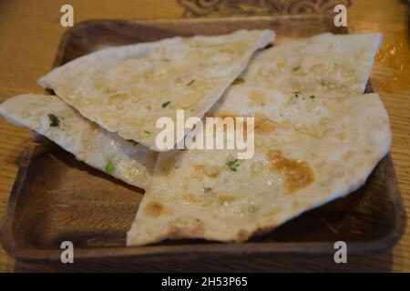 Naan all'aglio, popolare focaccia indiana, servito in un piatto di legno Foto Stock