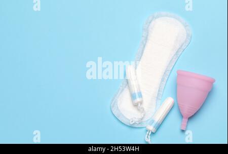 Mestruazioni. Igiene per mestruazioni, tamponi, tamponi e una ciotola per mestruazioni su sfondo blu. Foto Stock