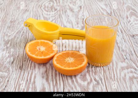 Un bicchiere di succo appena spremuto, metà di un mandarino maturo e una centrifuga a mano si trovano su un tavolo di legno, vicino, profondità di campo poco profonda Foto Stock