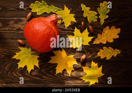 Zucca rossa e foglie d'autunno su sfondo di legno scuro, giacitura piatta Foto Stock