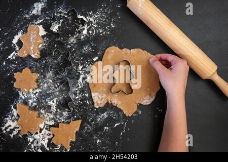 Le mani dei bambini fanno i biscotti del pan di zenzero di Capodanno su un tavolo di legno. Capodanno e Natale. Foto Stock