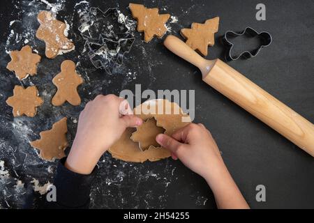 Le mani dei bambini fanno i biscotti del pan di zenzero di Capodanno su un tavolo di legno. Capodanno e Natale. Foto Stock