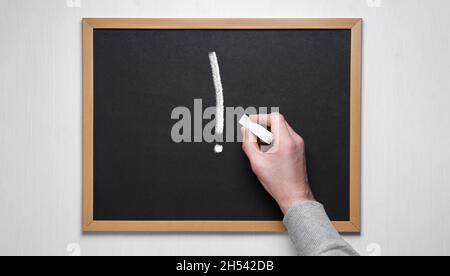 Mano che tiene gesso su blackboard.exclamation punto su un bordo del gesso. Foto Stock