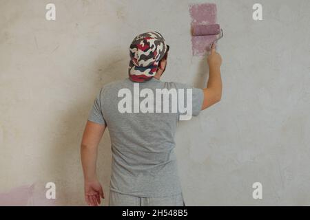 La vista posteriore di un giovane adulto dipinge la parete con un rullo. Riparazione in casa con le proprie mani Foto Stock