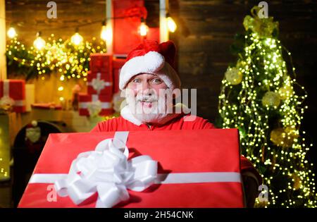 Uomo felice in costume di santa con regalo di Natale. Sorridendo Babbo Natale con grande regalo. Servizio di consegna. Foto Stock