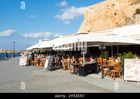 Chania, Creta - Grecia - Ottobre 20 2021 : incantevole taverna sul marciapiede presso lo storico porto veneziano i turisti godono del sole estivo Paesaggio Foto Stock