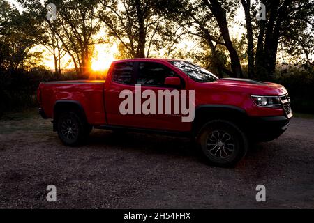 2019 Chevrolet Colorado ZR2 di fronte al tramonto con alberi in silhouette parcheggiati su ghiaia con cespugli, cielo pallido che attraversa Foto Stock