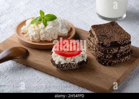 Fette di pane di segale con formaggio casereccio e pomodoro su piatto di legno Foto Stock