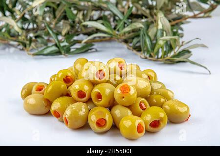 Piccole olive verdi in salamoia, farcite con peperoncino rosso in una ciotola di legno. Frutta di Olea europaea, farcita con fette di peperone. Primo piano da abov Foto Stock