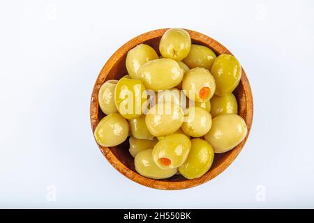 Piccole olive verdi in salamoia, farcite con peperoncino rosso in una ciotola di legno. Frutta di Olea europaea, farcita con fette di peperone. Primo piano da abov Foto Stock