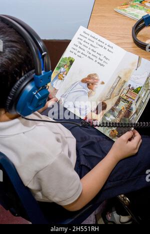 St.Paul, Minnesota. Scuola charter per l'Hmong. classe di lettura di 2° grado. Hmong studente che ascolta la versione audio del libro. Foto Stock