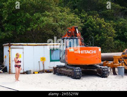 SARBINOWO, POLONIA - 02 ago 2016: L'escavatore Hitachi e la donna in piedi sulla sabbia accanto ad un container in una spiaggia Foto Stock