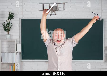 Ritratto di eccitata linea di insegnamento degli insegnanti senior degli studenti delle scuole superiori con computer portatile in aula su lavagna. Stupito maschio anziano in pensione Foto Stock