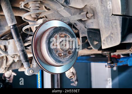 Il vecchio disco del freno posteriore di una vettura è usurato sul supporto di sollevamento o riparazione presso la stazione di servizio. Foto Stock