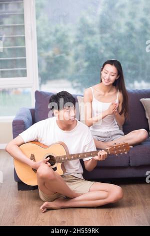 Giovane che suona la chitarra per la sua ragazza in soggiorno Foto Stock