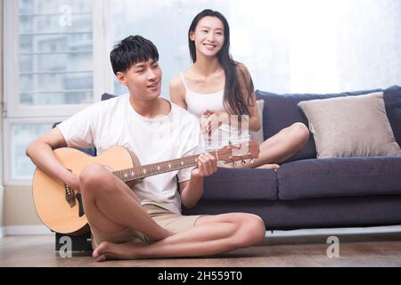 Giovane che suona la chitarra per la sua ragazza in soggiorno Foto Stock