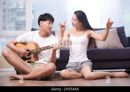 Giovane che suona la chitarra per la sua ragazza in soggiorno Foto Stock